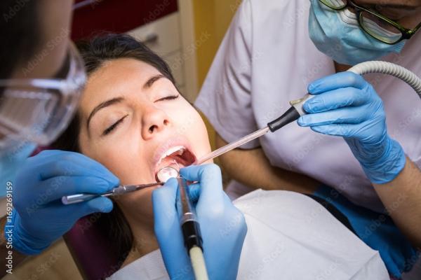 Woman in cabinet with eyes closed during procedure made by dentist and assistant.